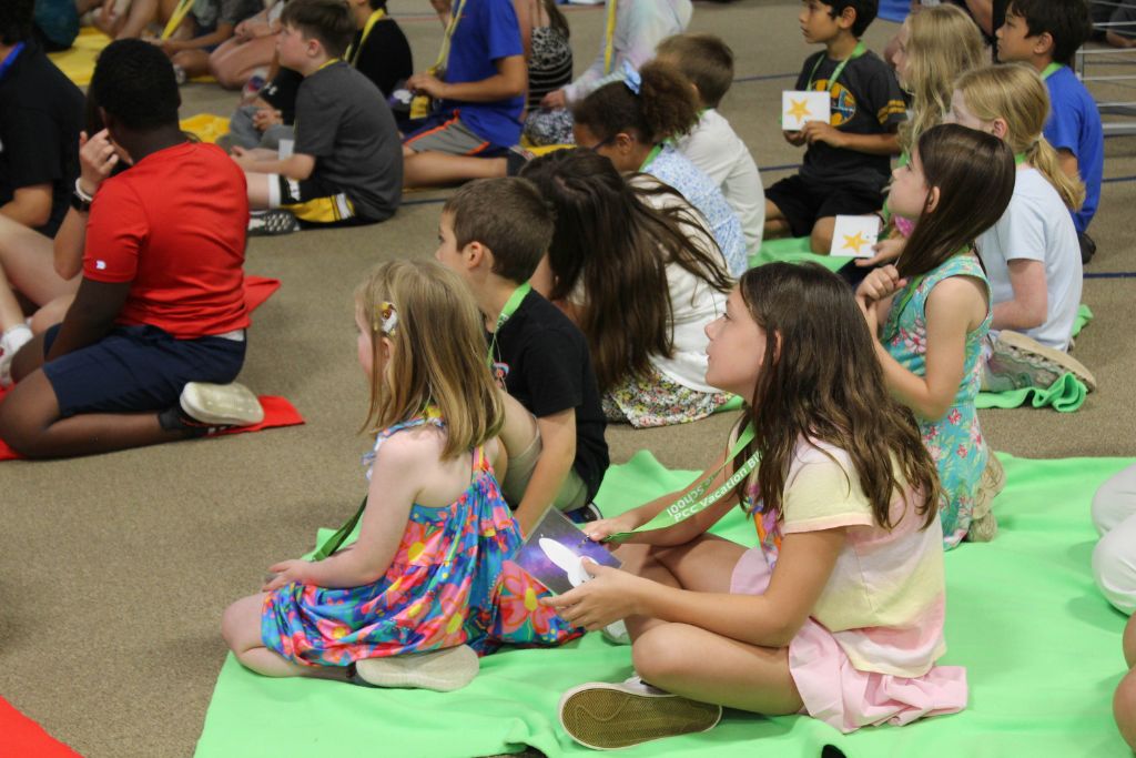 A group of children sit on the floor listening.